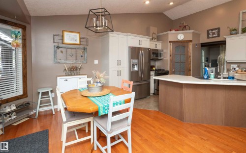 Vaulted ceiling with recessed lighting, wood-finish flooring, stainless steel appliances, light-toned cabinetry, and a kitchen island with seating - 6003 50 Ave, Barrhead, AB 