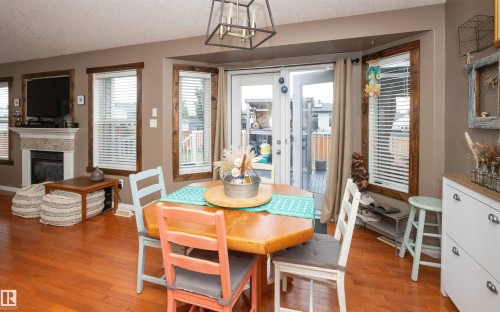 Hardwood flooring, fireplace with stone surround, white mantel, transom window, and double doors to outdoor space - 6003 50 Ave, Barrhead, AB 