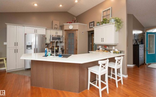 Kitchen featuring an angled island with a built-in sink, stainless steel appliances, white cabinetry, and wood-finish flooring - 6003 50 Ave, Barrhead, AB 