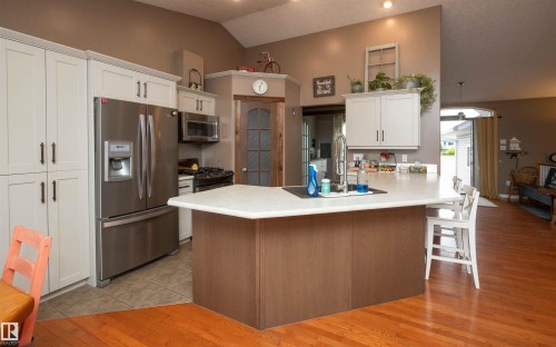 Kitchen featuring vaulted ceilings, wood-finish flooring, stainless steel appliances, and an island with countertop seating - 6003 50 Ave, Barrhead, AB 