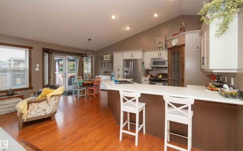 Wood-finish flooring throughout, vaulted ceiling, kitchen island with seating, stainless steel appliances, and sliding glass doors to outdoor area - 6003 50 Ave, Barrhead, AB 