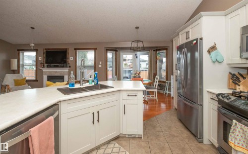 Kitchen featuring white shaker-style cabinetry, stainless steel appliances, a corner island with a double sink, and a tile floor - 6003 50 Ave, Barrhead, AB 