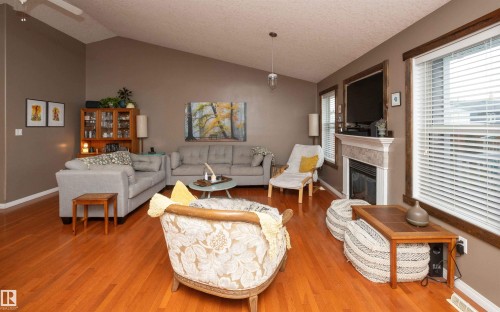 Vaulted ceiling with a ceiling fan, wood-finish flooring, built-in fireplace with a mantel, and multiple windows with blinds - 6003 50 Ave, Barrhead, AB 