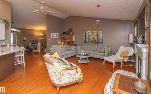 Vaulted ceiling with a ceiling fan, wood-finish flooring, fireplace with a mantel, and a kitchen island with a light-toned countertop - 6003 50 Ave, Barrhead, AB 