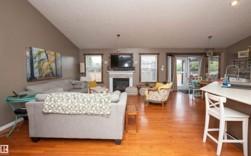 Vaulted ceiling, wood-finish flooring, fireplace with mantel, built-in kitchen island with sink, and double glass patio doors - 6003 50 Ave, Barrhead, AB 