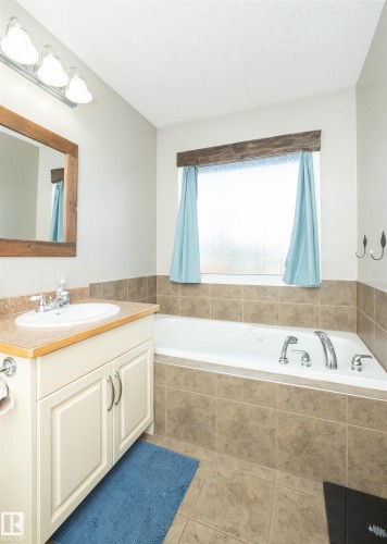 Built-in soaking tub, single vanity with light wood-finish countertop, tile flooring, and wall-mounted light fixture - 6003 50 Ave, Barrhead, AB 
