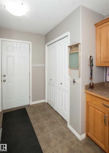 Entry area featuring square tile flooring, a built-in storage closet with bi-fold doors, and a wood-finish cabinet with a countertop - 6003 50 Ave, Barrhead, AB 
