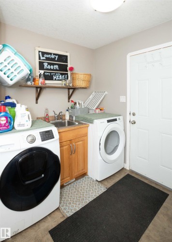 Dedicated laundry room featuring a utility sink with wood cabinetry, light-toned walls, and a ceiling-mounted light fixture - 6003 50 Ave, Barrhead, AB 