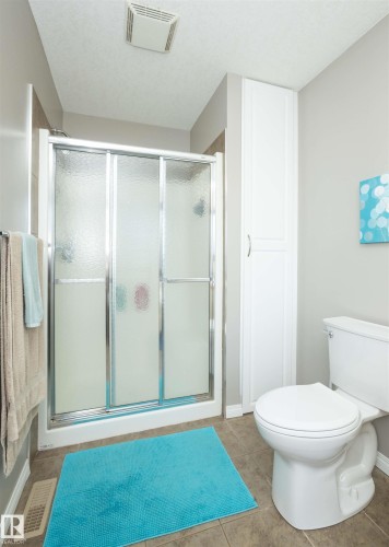 Frosted glass shower enclosure, white built-in storage cabinet, white toilet, and neutral tile flooring - 6003 50 Ave, Barrhead, AB 