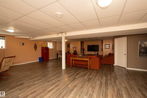 Expansive lower-level space featuring wood-finish flooring, drop ceiling with recessed lighting, and a white paneled door - 6003 50 Ave, Barrhead, AB 