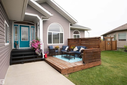 Front exterior featuring horizontal siding, an arched window, a vibrant front door with decorative glass inserts, and a wooden deck - 6003 50 Ave, Barrhead, AB 