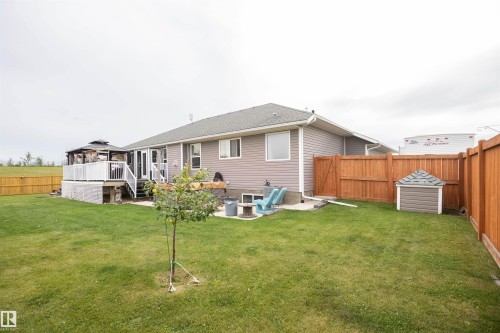 Expansive backyard featuring a manicured lawn, a multi-level deck with a gazebo, wood privacy fencing, and a compact storage shed - 6003 50 Ave, Barrhead, AB 