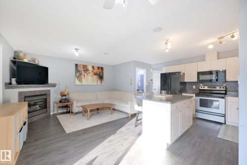Open-concept living space featuring wood-finish flooring, a tiled fireplace, and a kitchen island with seating - 8127 7 Avenue Sw, Edmonton, AB 