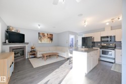 Open-concept living space featuring wood-finish flooring, a tiled fireplace, and a kitchen island with seating - 