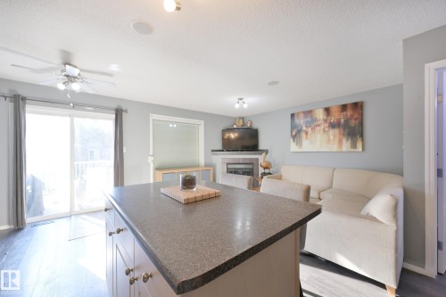 Kitchen island with a dark countertop, white cabinetry with brass hardware, wood-finish flooring, sliding glass door, and a fireplace with a mantel - 8127 7 Avenue Sw, Edmonton, AB 