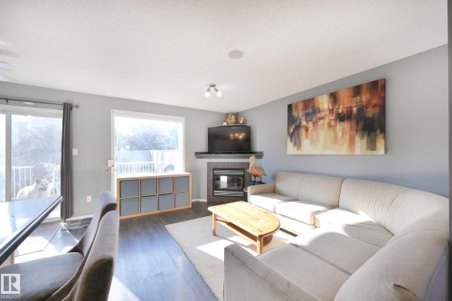 Living space featuring wood-finish flooring, a built-in fireplace, and expansive windows - 8127 7 Avenue Sw, Edmonton, AB 