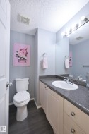 Wood-finish flooring, white vanity with paneled doors, built-in sink, gray countertop, and overhead vanity lighting - 