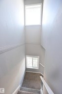 Carpeted staircase with white handrails and two windows providing natural light - 