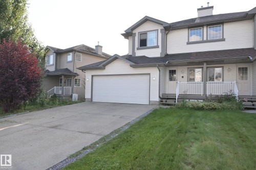 Exterior featuring light-toned siding, attached garage, concrete driveway, and covered front entry - 8127 7 Avenue Sw, Edmonton, AB 
