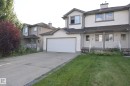 Exterior featuring light-toned siding, attached garage, concrete driveway, and covered front entry - 8127 7 Avenue Sw, Edmonton, AB 