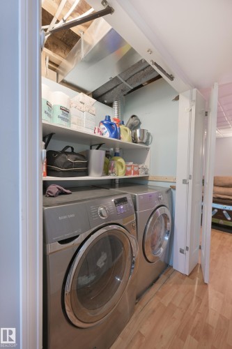 Laundry area featuring a front-loading washer and dryer, wood-finish flooring, and built-in shelving - 8127 7 Avenue Sw, Edmonton, AB 