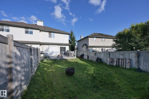 Expansive grassy yard with a wooden fence boundary, featuring a rear deck with white railings and sliding glass doors - 8127 7 Avenue Sw, Edmonton, AB 