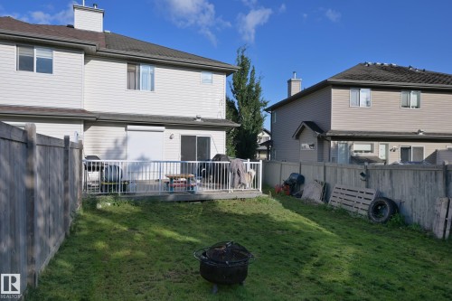 Rear exterior featuring a ground-level deck with white railing, sliding glass door, and upper-level windows - 8127 7 Avenue Sw, Edmonton, AB 