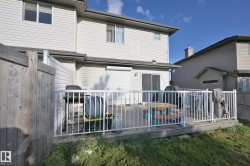 Rear wood-finish deck with white railings, featuring a sliding glass door and privacy fencing - 
