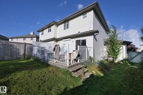 Private fenced backyard featuring a raised deck with white railings and a sliding glass door entry - 8127 7 Avenue Sw, Edmonton, AB 