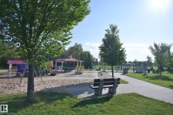 Expansive outdoor area featuring a sand-based play structure, covered gazebo with picnic tables, paved walking paths, and mature trees - 