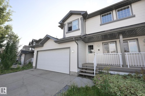 Light-toned siding exterior with dark trim accents, a single-car garage, and a covered front porch with white railings - 8127 7 Avenue Sw, Edmonton, AB 