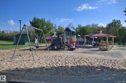 Sand-covered play area featuring a swing set, multi-level play structure, and covered seating area - 