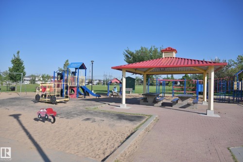 Community playground featuring multiple play structures, a covered picnic area with built-in tables, and expansive sand areas - 8127 7 Avenue Sw, Edmonton, AB 