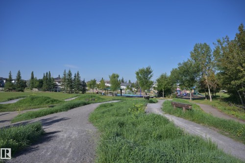 Expansive parkland featuring walking paths, mature trees, open grassy areas, and a visible play structure - 8127 7 Avenue Sw, Edmonton, AB 