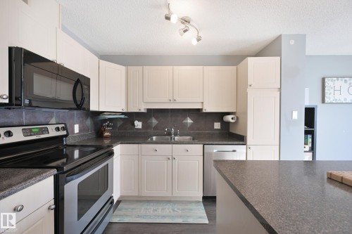 White cabinetry, dark countertops, built-in microwave, stainless steel range, and track lighting - 8127 7 Avenue Sw, Edmonton, AB 