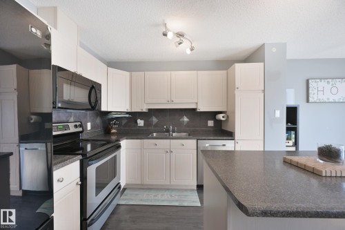 Kitchen featuring white cabinetry, stainless steel appliances, dark countertops, a tile backsplash, and dark wood-finish flooring - 8127 7 Avenue Sw, Edmonton, AB 