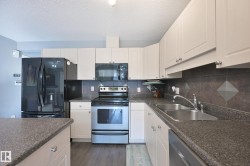 Kitchen featuring white cabinetry, dark speckled countertops, a dark tile backsplash, a double basin stainless steel sink, and wood-finish flooring - 