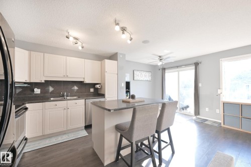 Kitchen featuring white cabinetry, dark countertops, and a central island with bar seating - 8127 7 Avenue Sw, Edmonton, AB 