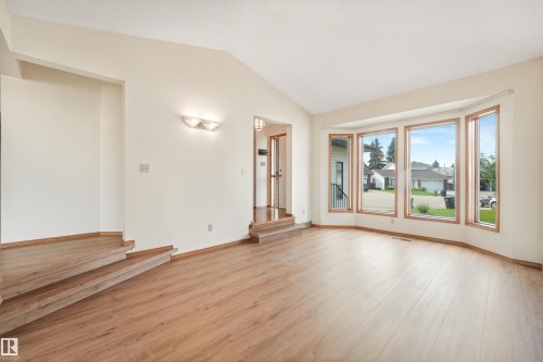 Expansive living area featuring a prominent bay window, wood-finish flooring, a vaulted ceiling, and an integrated wall sconce - 8008 158 Avenue Nw, Edmonton, AB - Indoor Photo Showing Other Room