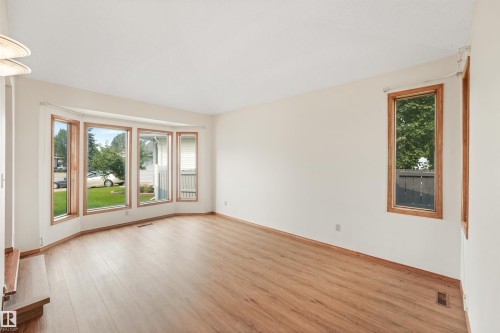 Spacious living area featuring a prominent bay window with wood-finish trim, wood-finish flooring, and light-toned walls - 8008 158 Avenue Nw, Edmonton, AB - Indoor Photo Showing Other Room