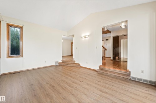 Spacious room featuring wood-finish flooring, a vaulted ceiling, and an accent wall sconce - 8008 158 Avenue Nw, Edmonton, AB - Indoor Photo Showing Other Room