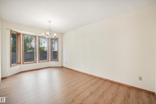 Bay window with dark wood-finish trim, wood-finish flooring, neutral wall paint, and a multi-bulb chandelier - 8008 158 Avenue Nw, Edmonton, AB - Indoor Photo Showing Other Room