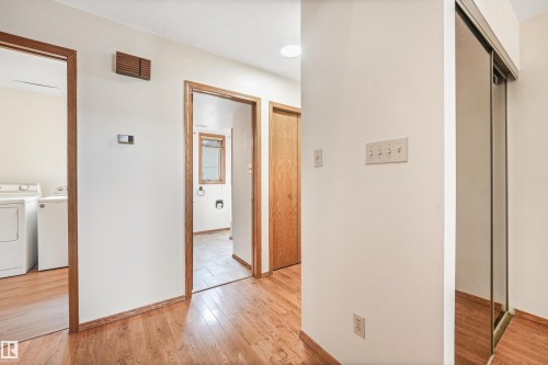 Hallway featuring wood-finish flooring, white walls, and wood trim around doorways - 8008 158 Avenue Nw, Edmonton, AB - Indoor
