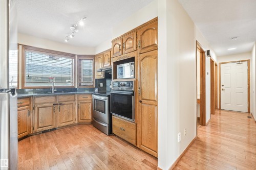 Kitchen featuring wood cabinetry, stainless steel appliances, dark countertops, and a bay window - 8008 158 Avenue Nw, Edmonton, AB - Indoor Photo Showing Kitchen