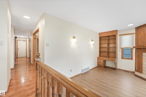 Interior space featuring wood-finish flooring, built-in shelving with integrated desk, and a wooden railing - 8008 158 Avenue Nw, Edmonton, AB - Indoor Photo Showing Other Room With Fireplace