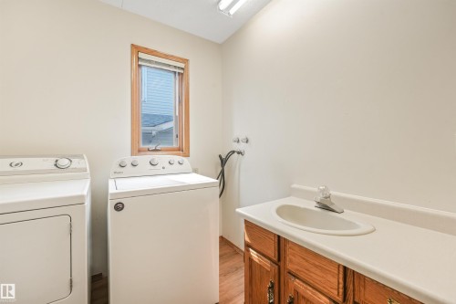 Dedicated laundry area featuring a window with wood trim, wood-finish flooring, and a built-in vanity with cabinetry and an integrated sink - 8008 158 Avenue Nw, Edmonton, AB - Indoor Photo Showing Laundry Room