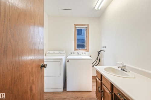 Dedicated laundry space featuring wood-finish flooring, a utility sink with a white countertop, and built-in wood cabinetry - 8008 158 Avenue Nw, Edmonton, AB - Indoor Photo Showing Laundry Room