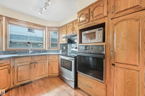 Kitchen featuring wood cabinetry, stone-look countertops, and stainless steel appliances including a built-in oven and microwave - 8008 158 Avenue Nw, Edmonton, AB - Indoor Photo Showing Kitchen With Double Sink