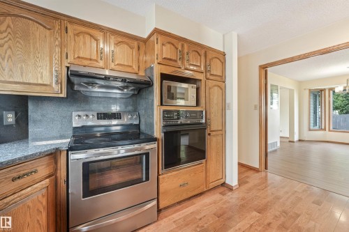 Kitchen featuring wood-finish cabinetry, stainless steel range with overhead vent, and a built-in microwave and oven combination - 8008 158 Avenue Nw, Edmonton, AB - Indoor Photo Showing Kitchen