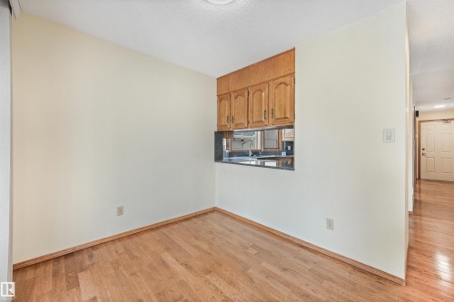 Room featuring wood-finish flooring, white painted walls, and a pass-through window with a dark countertop - 8008 158 Avenue Nw, Edmonton, AB - Indoor Photo Showing Other Room